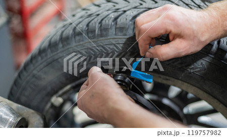 A mechanic attaches balancing weights to a wheel.  119757982