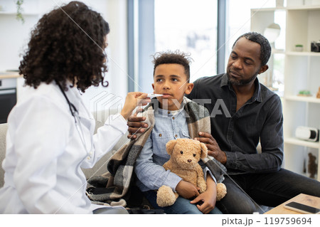 African female doctor checks temperature of young boy at home 119759694