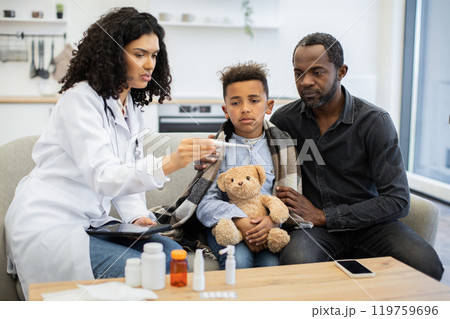 African female doctor checking temperature of a young boy at home 119759696