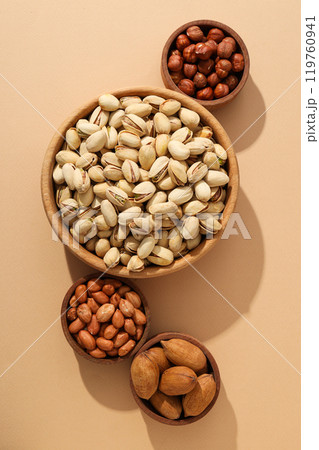 Various nuts in wooden bowls on a beige background Various nuts in wooden bowls on a beige background 119760941