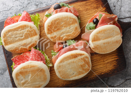 Small italian tigelle sandwiches with sausage, jamon and fresh vegetables close-up on wooden board. Horizontal top view Small italian tigelle sandwiches with sausage, jamon and fresh vegetables close-up on wooden board. Horizontal top view 119762010