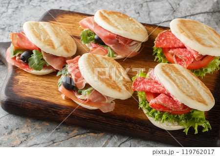 Small italian tigelle sandwiches with sausage, jamon and fresh vegetables close-up on wooden board. Horizontal Small italian tigelle sandwiches with sausage, jamon and fresh vegetables close-up on wooden board. Horizontal 119762017