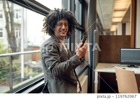 Smiling young man near the window with a phone in hands 119762067