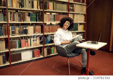 Curly-haired young man studying in the library and looking involved 119762162