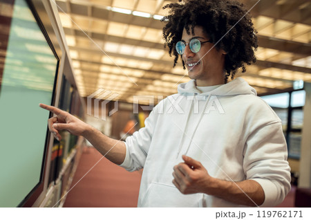 Curly-haired young man standing near the screen in the library and searching a book 119762171