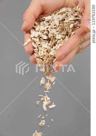 Hands pouring uncooked raw oatmeal on a gray background. Hands pouring uncooked raw oatmeal on a gray background. 119762280