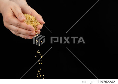 Hands pouring raw uncooked bulgur cereals on a black background space for text 119762282