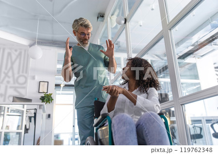 Male doctor carrying a wheelchair with a female patient 119762348