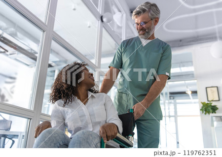 Male doctor carrying a wheelchair with a female patient 119762351
