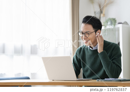 ノートパソコンでビデオ通話をするイヤホンをつけた30代後半の男性 ノートパソコンでビデオ通話をするイヤホンをつけた30代後半の男性 119762837