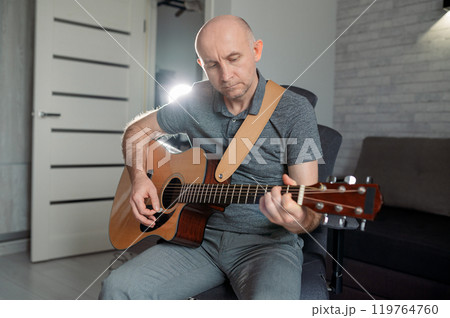 Guitarist paying a acoustic guitar in office. portrait Male musician sitting on sofa and playing music instrument Guitarist paying a acoustic guitar in office. portrait Male musician sitting on sofa and playing music instrument 119764760