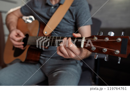 Guitarist paying a acoustic guitar in office. portrait Male musician sitting on sofa and playing music instrument Guitarist paying a acoustic guitar in office. portrait Male musician sitting on sofa and playing music instrument 119764761