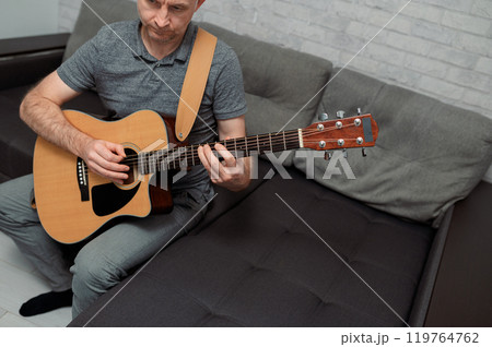 Guitarist paying a acoustic guitar in office. portrait Male musician sitting on sofa and playing music instrument Guitarist paying a acoustic guitar in office. portrait Male musician sitting on sofa and playing music instrument 119764762