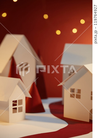 The Christmas picture in the red background, with an empty space to display products, is decorated next to white paper houses and red cones under the led string lights. 119764927