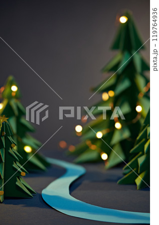 A strip of blue paper stretches out in the center, surrounded by green paper pines decorated with LED lights. Sample image with empty space to display products on a purple-blue backdrop. 119764936