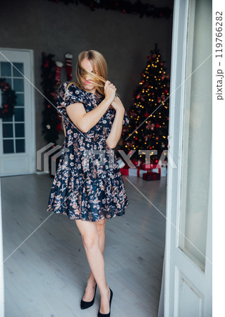 Blonde woman in dress smiling with gifts at Christmas tree for new year Blonde woman in dress smiling with gifts at Christmas tree for new year 119766282