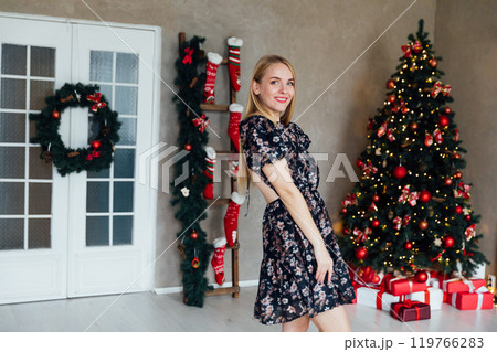 Blonde woman in dress smiling with gifts at Christmas tree for new year Blonde woman in dress smiling with gifts at Christmas tree for new year 119766283