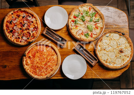 Assorted pizzas on a rustic wooden table, ready to serve with plates and cutlery Assorted pizzas on a rustic wooden table, ready to serve with plates and cutlery 119767052