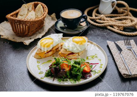 Gourmet breakfast with fried eggs on toast, cheddar, greens, and a side salad served with a latte 119767076
