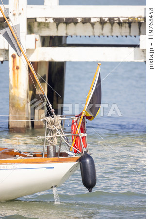 A beautiful sailboat is securely docked by the pier, accompanied by a buoy gently floating nearby A beautiful sailboat is securely docked by the pier, accompanied by a buoy gently floating nearby 119768458