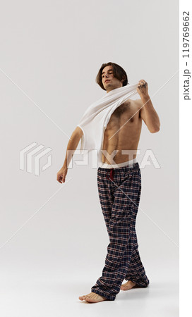 casual and relaxed. Man pulling off white shirt, creating dynamic, natural movement against white studio background. 119769662