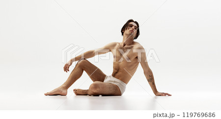 Man sitting on floor with calm, thoughtful expression against white studio background. . Emphasizes natural masculinity Man sitting on floor with calm, thoughtful expression against white studio background. . Emphasizes natural masculinity 119769686