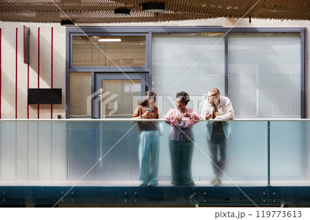 Wide angle shot of diverse group of three colleagues cheerfully chatting during break while standing on balcony in sunlight casting through glass ceiling in modern business center, copy space Wide angle shot of diverse group of three colleagues cheerfully chatting during break while standing on balcony in sunlight casting through glass ceiling in modern business center, copy space 119773613