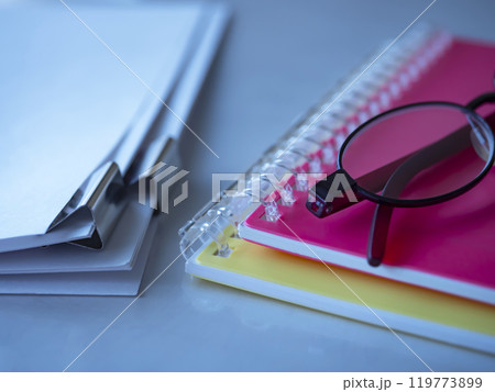 テーブルに置かれた書類と手帳とメガネ 119773899