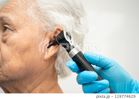 Otolaryngologist or ENT physician doctor examining senior patient ear with otoscope, hearing loss problem. 119774629