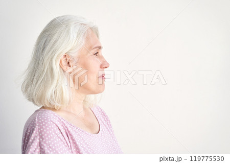 Profile of a contemplative elderly woman with gray hair in casual attire against 119775530