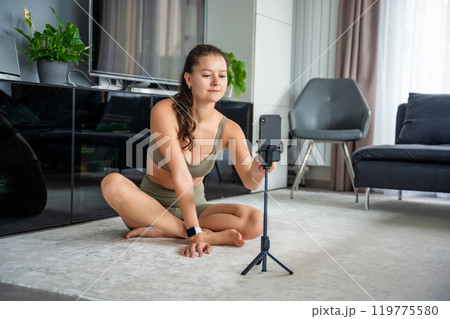 Young woman before doing sport exercise using a sports app on her mobile phone at home. Online training concept Young woman before doing sport exercise using a sports app on her mobile phone at home. Online training concept 119775580