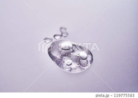 A drop of serum on a purple background. Texture of a cosmetic product. A drop of serum on a purple background. Texture of a cosmetic product. 119775583