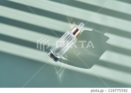 Bottle of cosmetic serum with pipette on green background with shadow stripes. 119775592