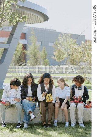 Vertical shot of young teacher giving robotics lesson to curious multiracial students under open sky in park 119775686