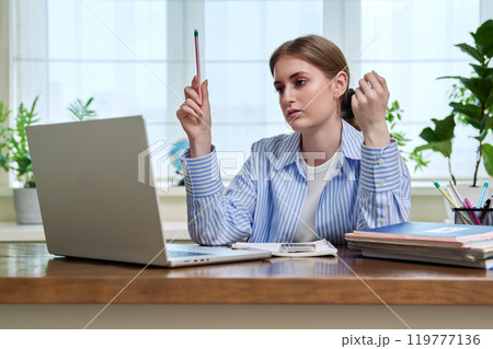 Teenage girl student studying online sitting at home at desk using laptop for video conference 119777136