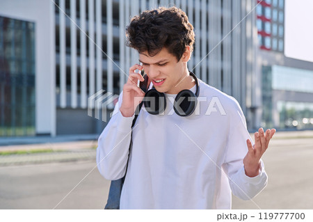 Young serious guy talking on mobile phone, modern city background, urban style Young serious guy talking on mobile phone, modern city background, urban style 119777700