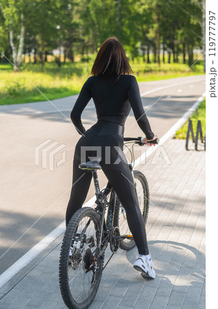 Rear view of Caucasian woman riding bike in park. Vertical photo. Rear view of Caucasian woman riding bike in park. Vertical photo. 119777797