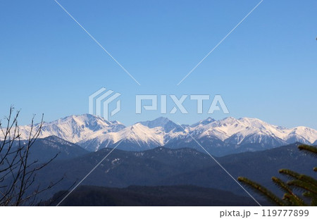 Snow-capped rocks and tree-covered mountains and hills of the Caucasus against a clear blue sky, view from an observation deck on the hills of the snowy mountains of Adygea Snow-capped rocks and tree-covered mountains and hills of the Caucasus against a clear blue sky, view from an observation deck on the hills of the snowy mountains of Adygea 119777899