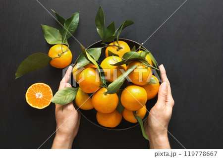 Fresh mandarins with leaves in female hand on black. Healthy eating concept. Copy space. Top view. Fresh mandarins with leaves in female hand on black. Healthy eating concept. Copy space. Top view. 119778667
