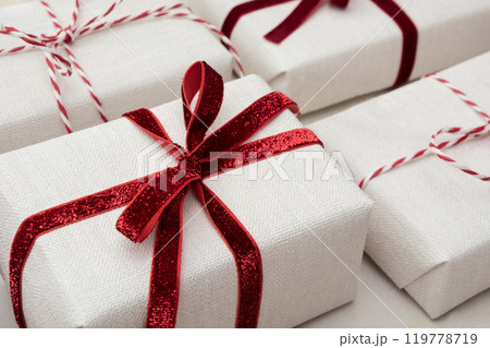 Christmas gift box wrapped in white craft paper and decorative red rope ribbon on marmoreal surface. Creative hobby, isometric. Close up. Christmas gift box wrapped in white craft paper and decorative red rope ribbon on marmoreal surface. Creative hobby, isometric. Close up. 119778719