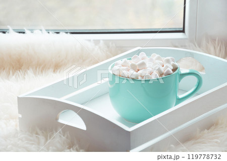 Blue cup of hot chocolate with marshmallow on windowsill with furskin for relax. Holiday concept. Home style. 119778732