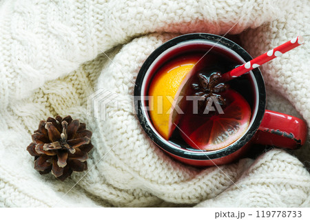 Christmas and winter traditional hot beverage. Mulled wine in red mug with spice wrapped in warm white scandinavian sweater. Christmas and winter traditional hot beverage. Mulled wine in red mug with spice wrapped in warm white scandinavian sweater. 119778733