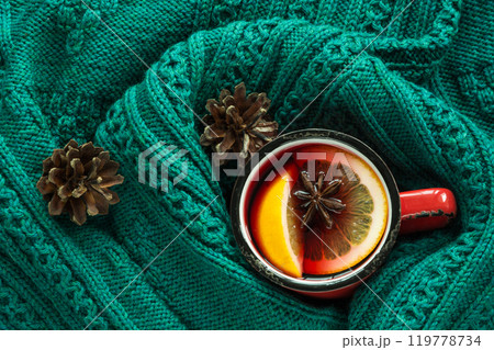 Christmas and winter traditional hot beverage. Mulled wine in red mug with spice wrapped in warm green scandinavian sweater. Christmas and winter traditional hot beverage. Mulled wine in red mug with spice wrapped in warm green scandinavian sweater. 119778734