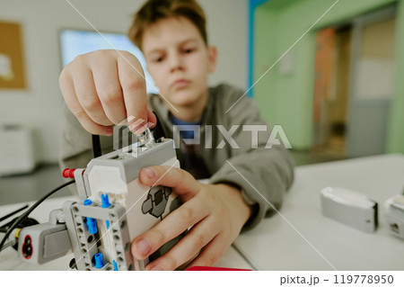 Medium close up of boys hand connecting wires to robot during robotics lesson Medium close up of boys hand connecting wires to robot during robotics lesson 119778950