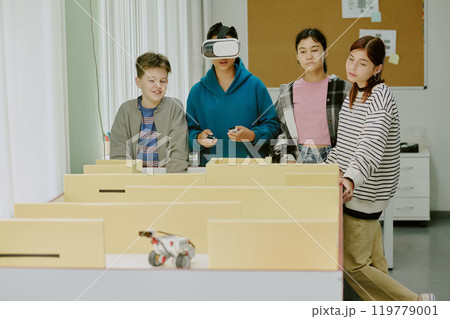 Boy in deep blue hoodie with VR headset surrounded by his classmates playing video game Boy in deep blue hoodie with VR headset surrounded by his classmates playing video game 119779001