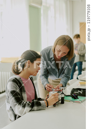 Vertical shot of young female teacher helping with robot wires while student holding robot carefully Vertical shot of young female teacher helping with robot wires while student holding robot carefully 119779108