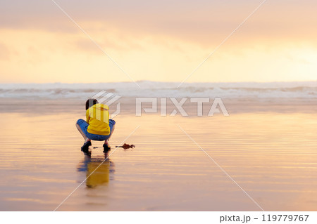 Teenager boy is sitting and enjoying solitude, exploring peaceful tranquil beach in sunset time, kelp seaweed on the sand. Tofino, Vancouver Island, Canada. 119779767