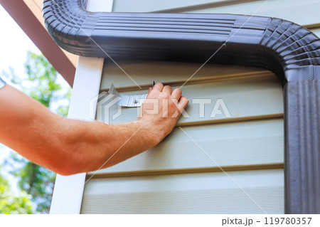 An worker is installing rain gutter on roof is fitting downpipe bending downspout 119780357