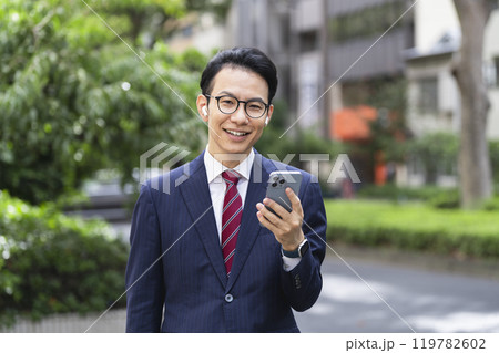 スマートフォンを持ったイヤホンをした30代後半のビジネスマン　カメラ目線 119782602