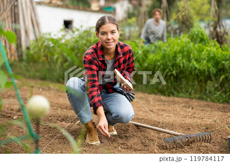 Positive girl buries berry and vegetable seeds in ground in garden bed 119784117